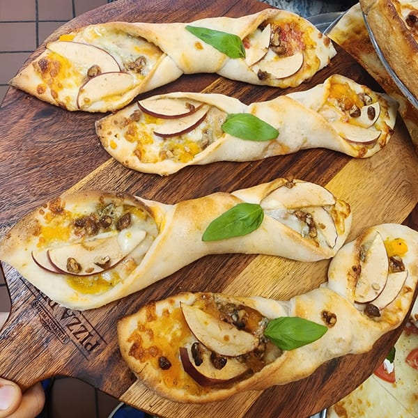 Four braided pizza twists with apples, walnuts, and basil on a wooden board at Pizza Village.