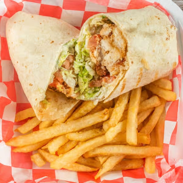 Chicken wrap with lettuce and tomatoes, served with a side of golden french fries in a red checkered basket.